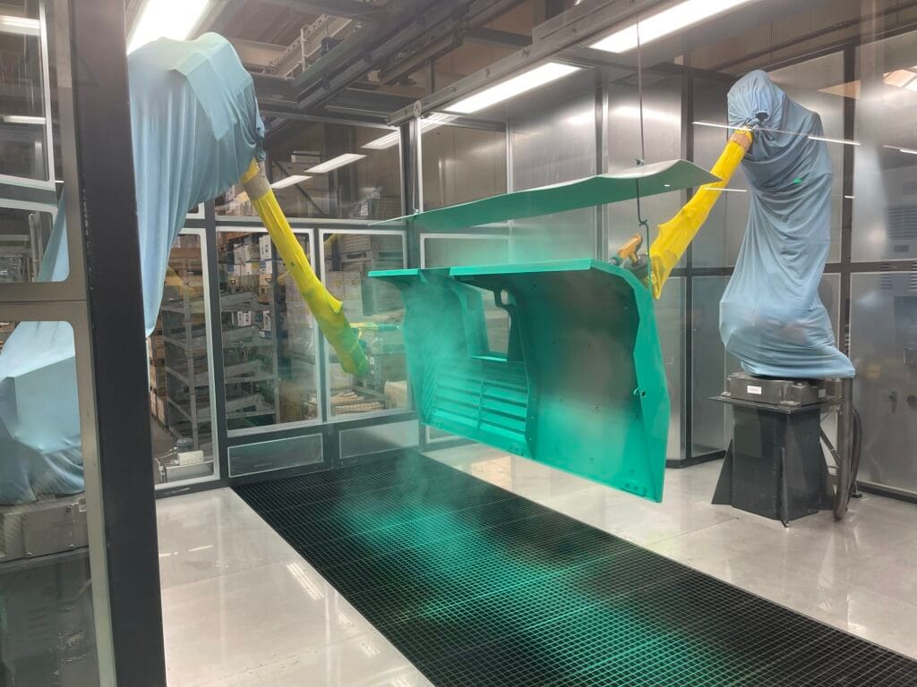 Robotic arms in blue protective covers operating inside a cleanroom, lifting a green container.
